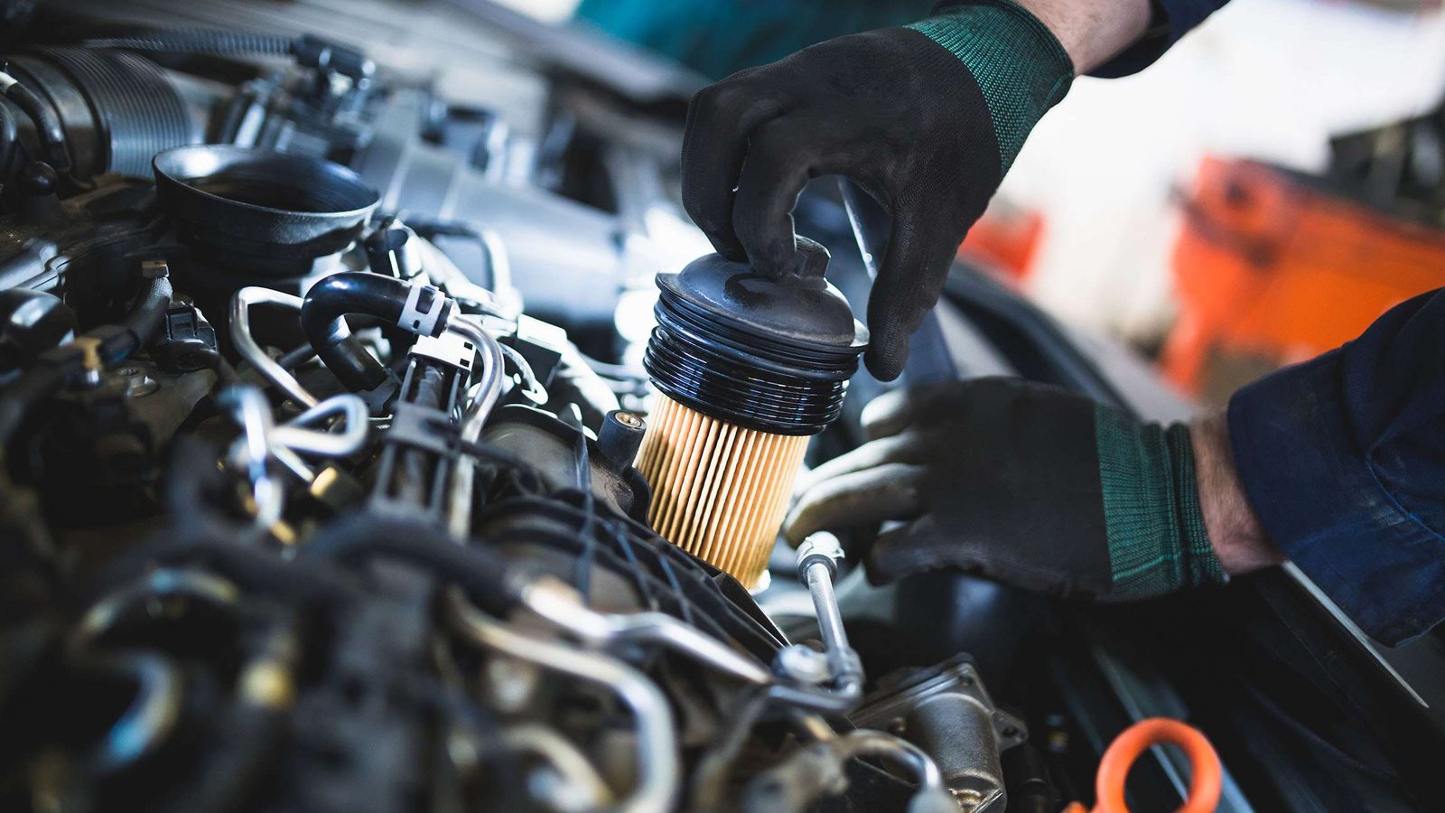 Stock photo: a mechanic in gloves fitting a new oil filter in a car engine bay.