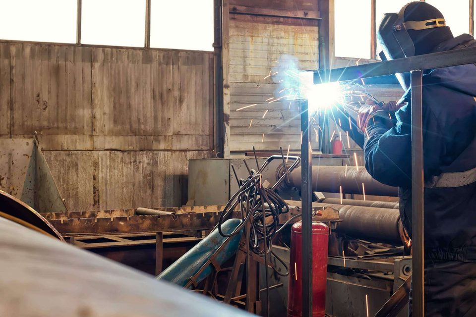 Stock photo: a welder in a mask welding steel supports in a fabrication shop.